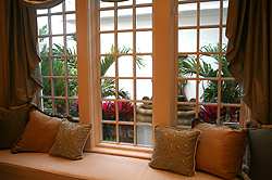 A simple yet elegant window treatment, color coordinated to provide a bit of contrast in the decor, lets plenty of sunlight in, making this window seat a great place to relax or read a book.