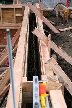Anchors to secure walls will be embedded in the top of the foundation walls while concrete is fresh. The slab will be poured over a vapor barrier between the foundation walls after they are completed.