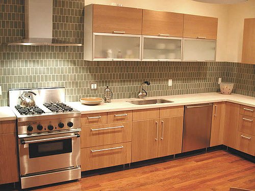 A modern style range hood and small, monotone tiles complete the contemporary look of this elegant kitchen.