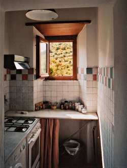 Small and practical, this humble kitchen in a Tuscan home shows a subtle use of brown, green and blue accent tiles that complement naturally finished wood and neutral stone tiles.